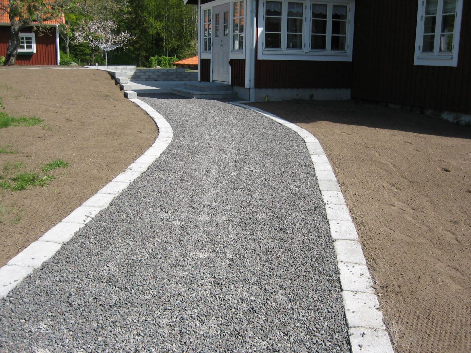 Böjd grusgång med stenkant mot rött bostadshus