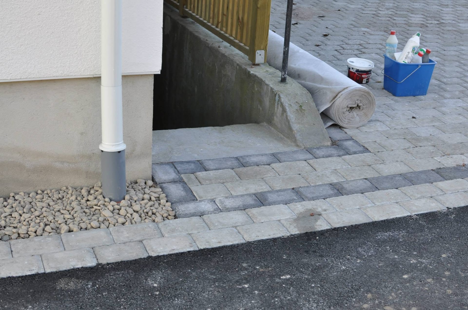 Stenläggning mot husgrund med singel och källarnedgång