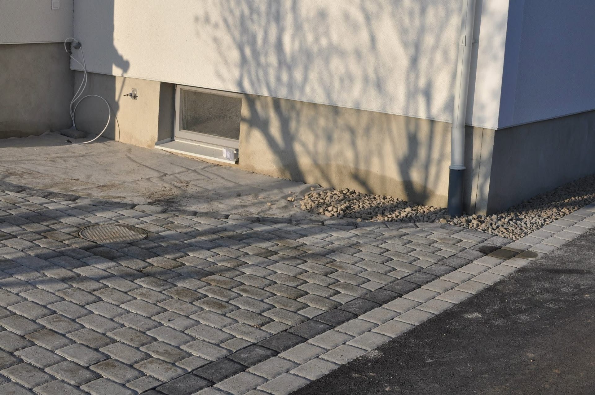 Stenlagd yta med brunnslock och förberedd remsa mot husgrund