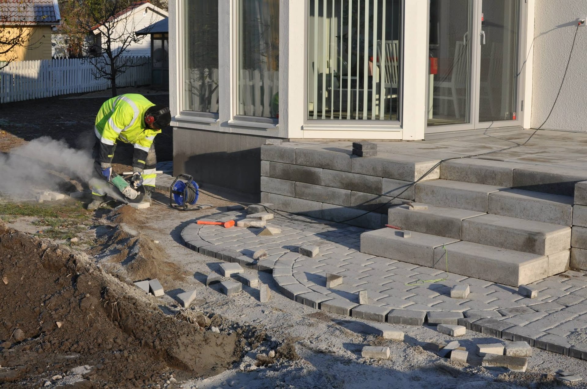 Arbetare som kapar plattor till en ny patio med trappa och stödmur